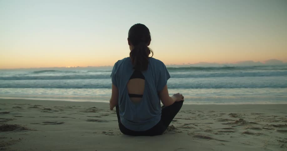 A girl walks on to a beach and sits down and looks at the water