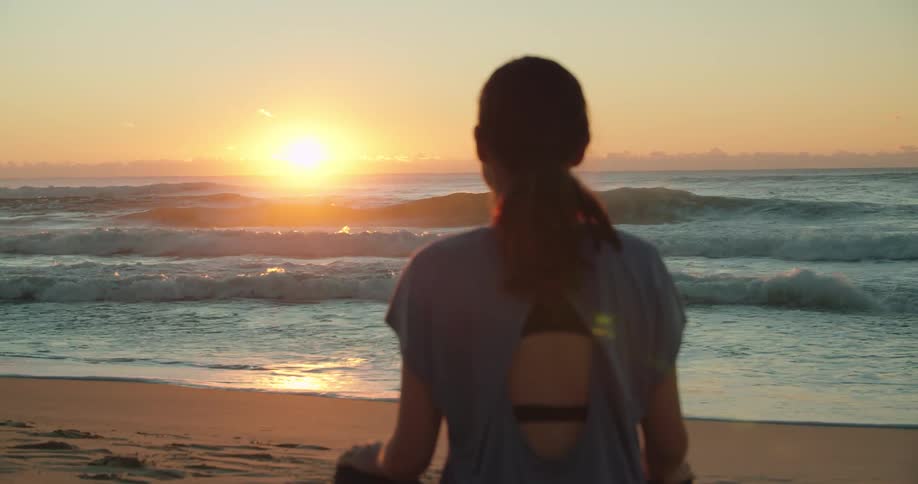 A woman meditating alone on a sandy beach at sunset