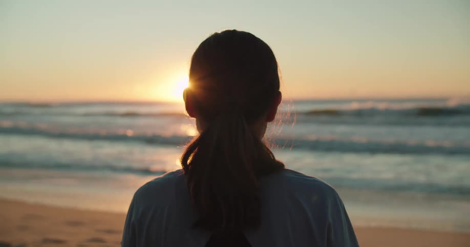 A silhouette of a woman standing on a beach with the sky and clouds in the background