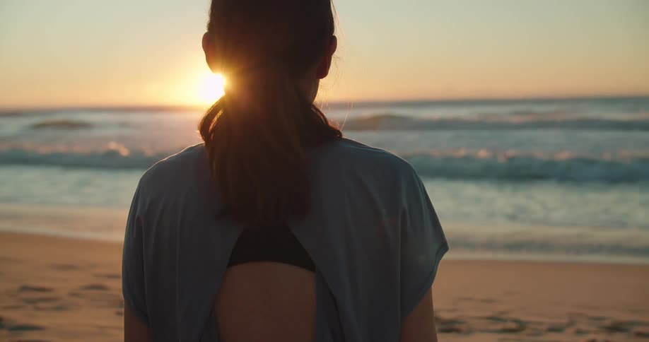 Woman sitting cross legged on the sand in front of the ocean at sunset