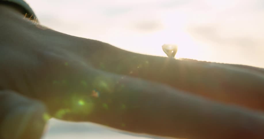 Engagement diamond ring on a hand in front of the ocean at sunset