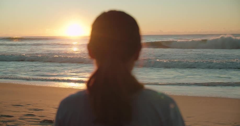 A woman standing alone on a sandy beach at sunset