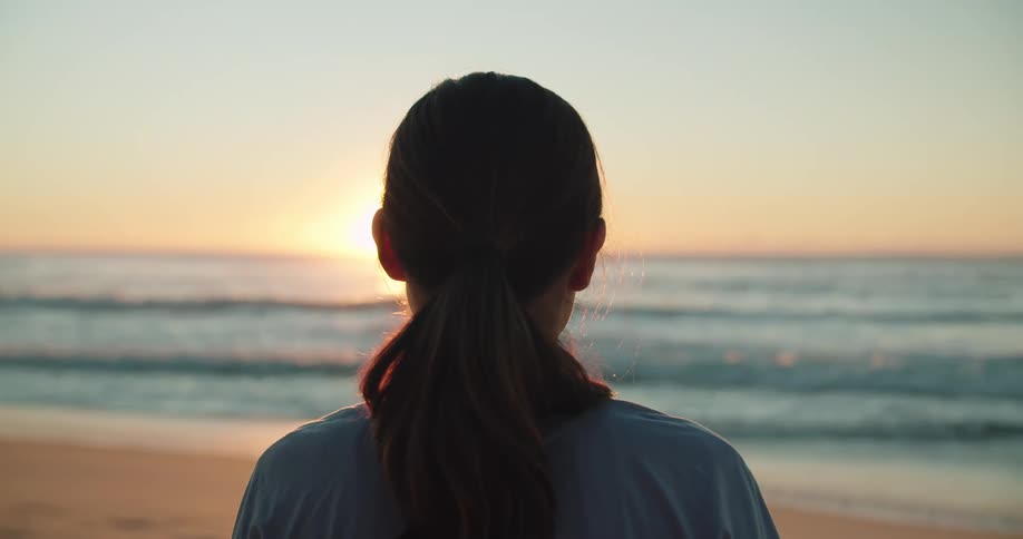 A woman is standing at the beach at dusk