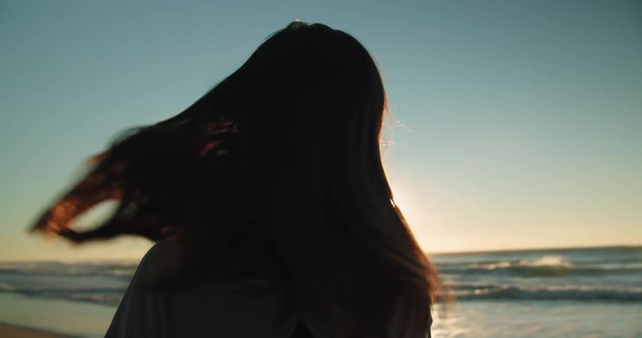 A woman waves her hair around on the beach