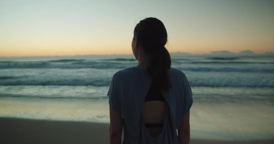 A woman is standing on the coast of an ocean at dusk