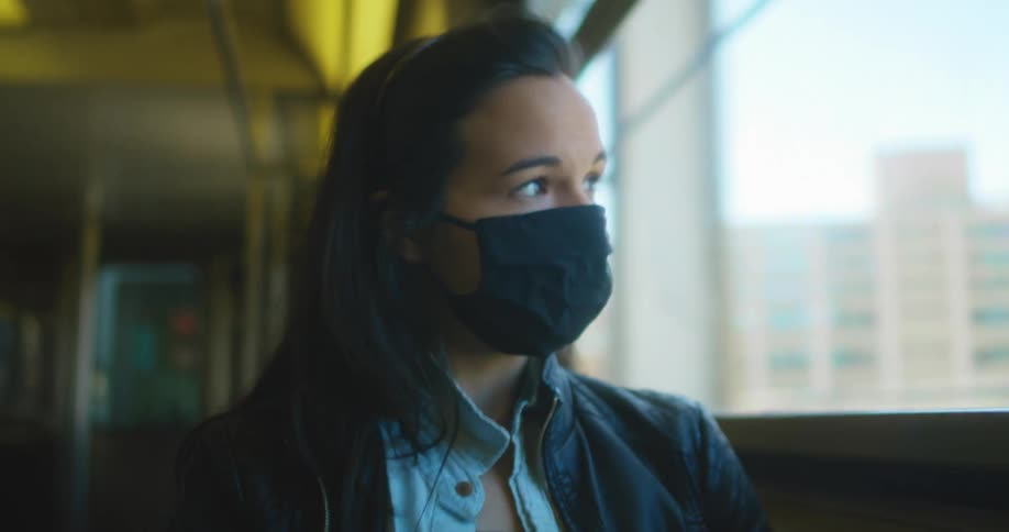 A woman sits on a bus with a mask on and looks out the window