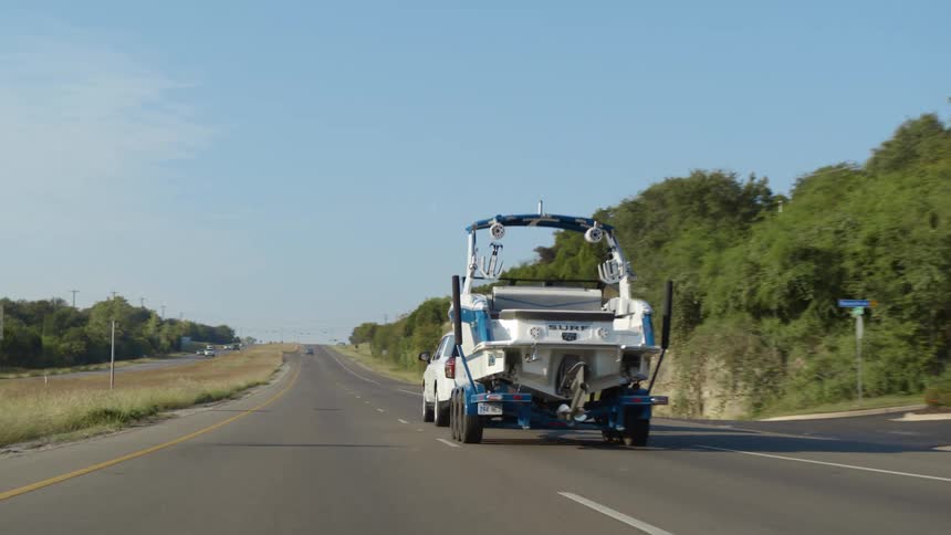 Suv pull boat trailer with motorboat down road through countryside past intersection