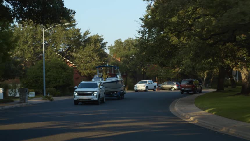 A white truck pulling a boat on a paved street in the daytime