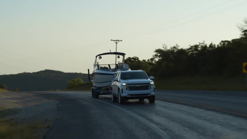 A white vehicle towing a boat on a rural paved road