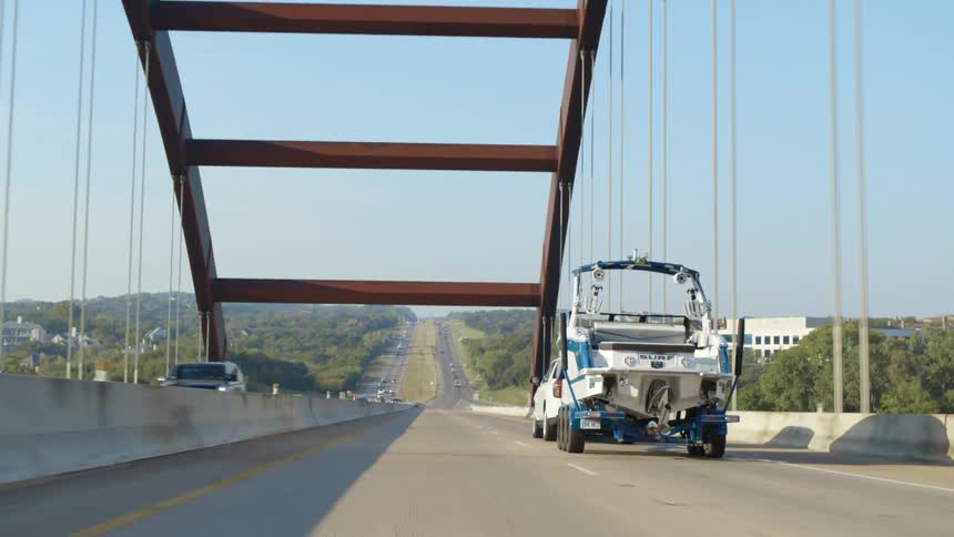 A sport utility vehicle tows a large motorboat on a trailer behind it while crossing a bridge