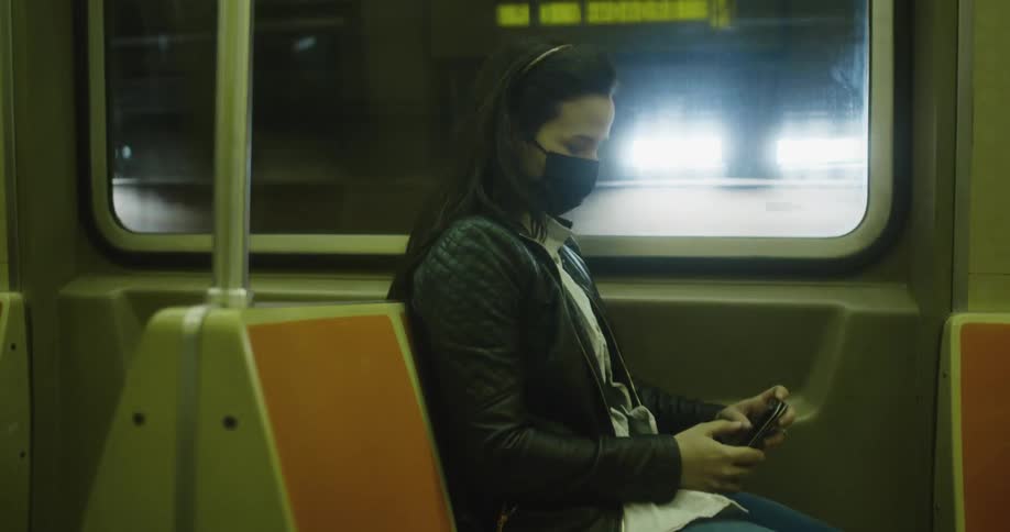 Woman wearing face mask sits in public transport texting on mobile phone