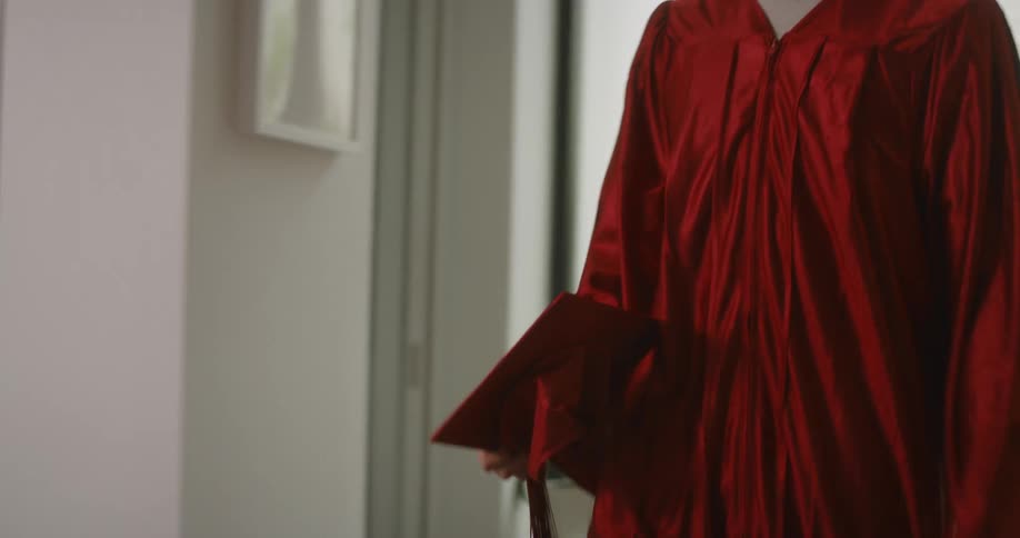 Graduate wearing a gown and carrying a graduation hat walks into a building and picks up a cowboy boot