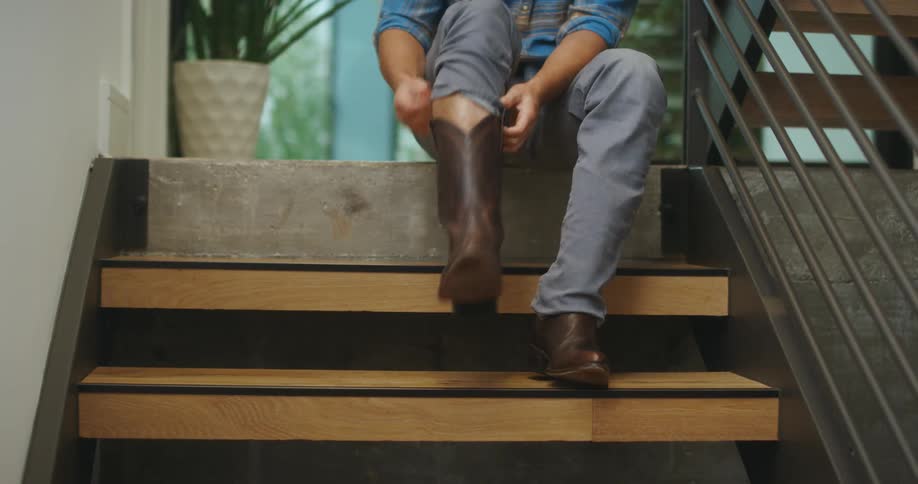 Man sitting on the staircase at home puts on a cowboy boots
