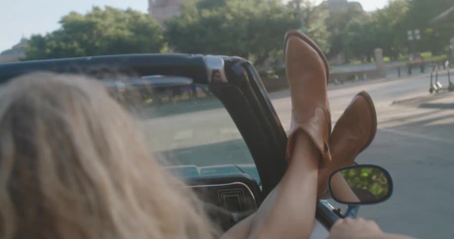 A woman riding in a convertible with her legs hanging out the window