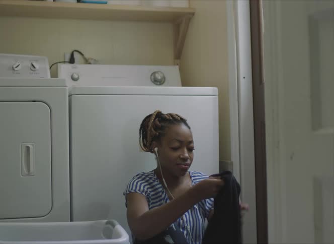 A woman folding laundry while sitting on the floor next to a washer and dryer