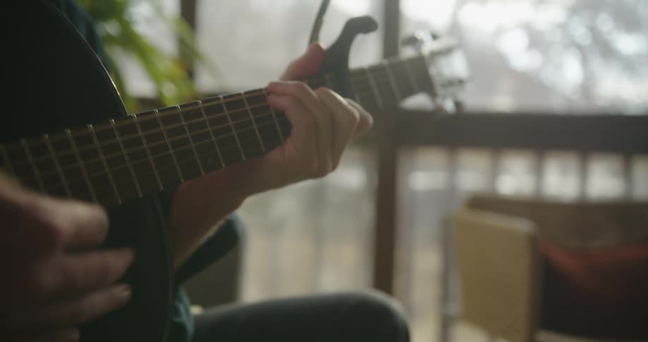 Man sitting on the living room playing acoustic guitar