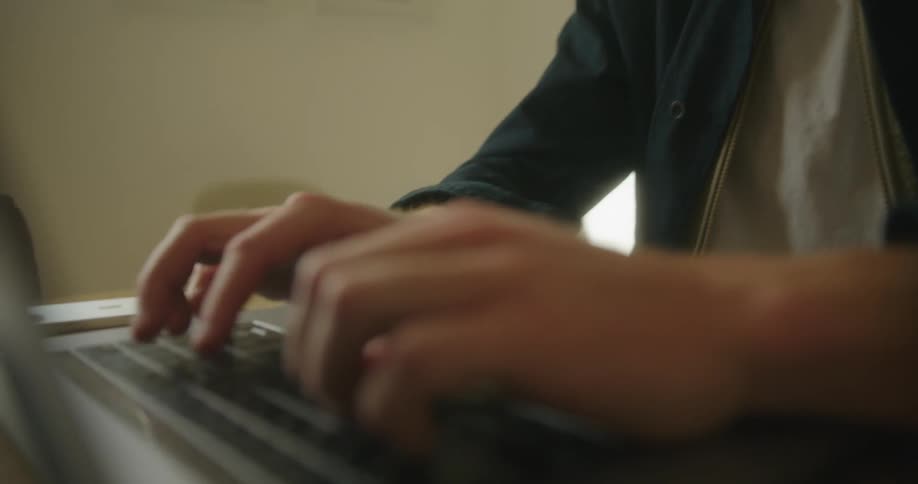 Blonde man sitting at table works on laptop in a room