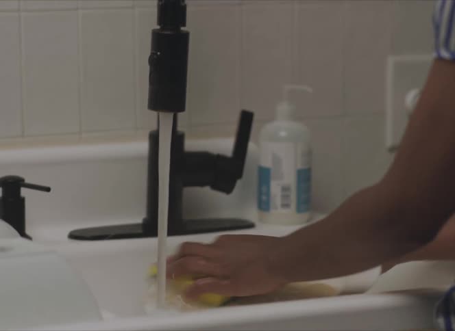 A woman wearing earbuds while washing dishes at a kitchen sink
