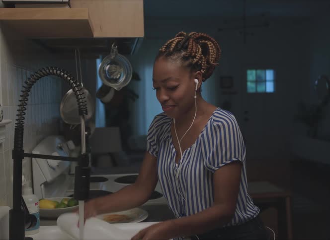 A woman is standing in her kitchen and washing dishes