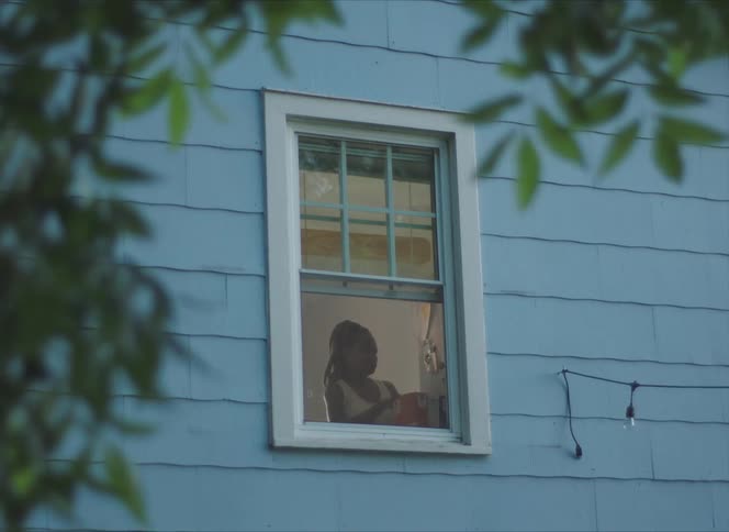 A woman seen through the window of a house with blue siding