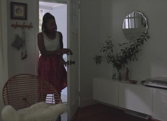 A woman entering a house by opening a door with a wall and a mirror in the background