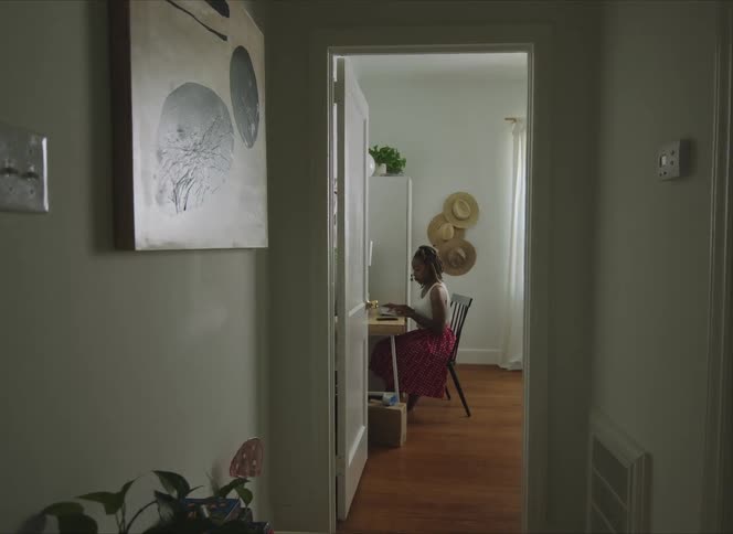 Woman sits at desk typing on computer keyboard near wall decorated with hats
