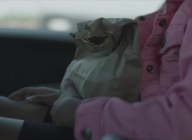 A child sitting on a moving car carrying a lunch bag on her lap