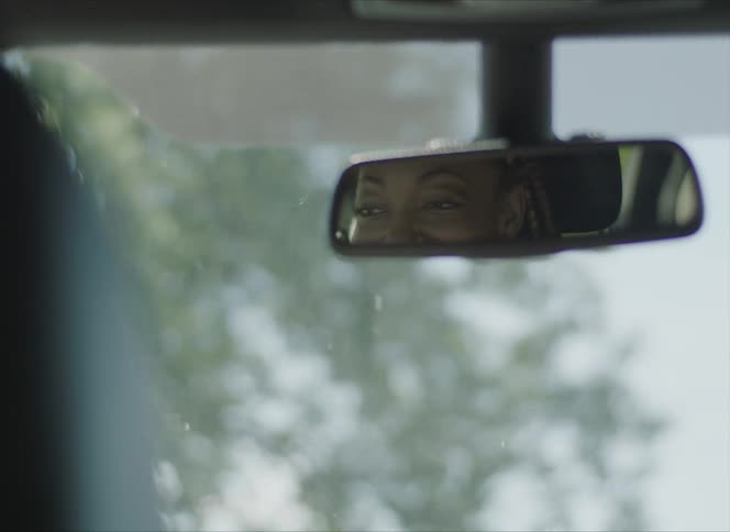 Woman smiles in rearview mirror as she drives under a blue sky