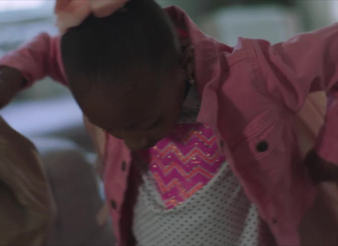Girl wearing pink jacket puts on pink backpack while holding brown bag lunch