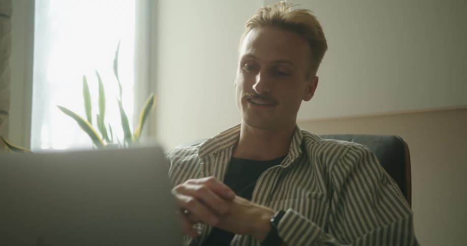 A man is sitting on a chair and looking at a laptop