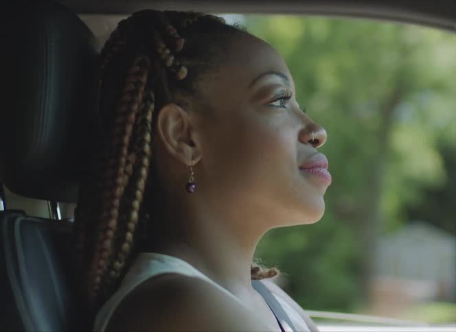 Woman with braids earrings and a white sleeveless shirt drives a car in the street
