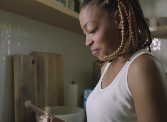 A woman in a room putting snacks into a brown paper bag with a wall in the background