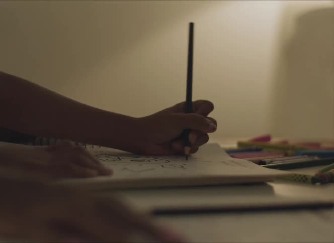 Person draws on paper with pencil on surface scattered with colors