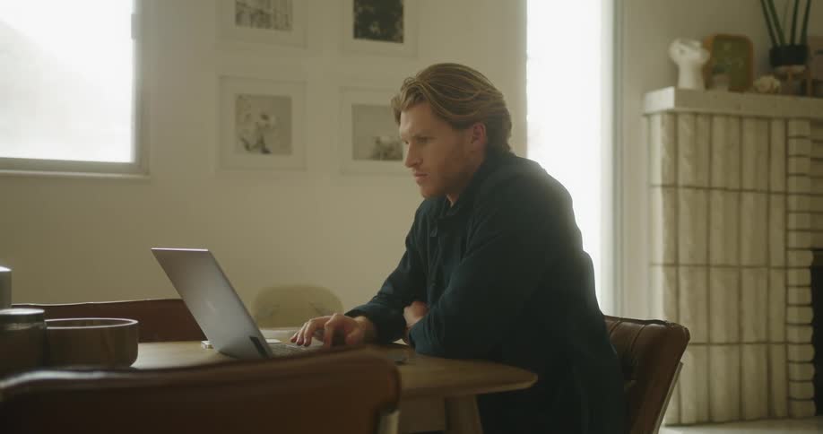 A man is typing on a laptop and sitting at a table
