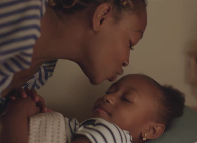 A woman tucks her daughter into bed and kisses her forehead