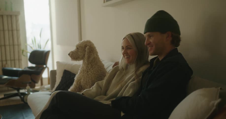 A man and woman are sitting on a couch with their dog