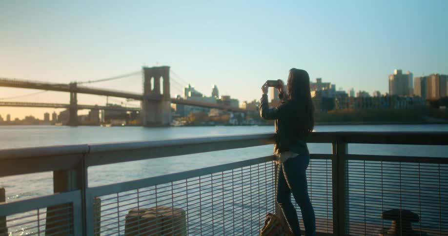 A teenage girl stands on the shore and takes photos with her cell phone