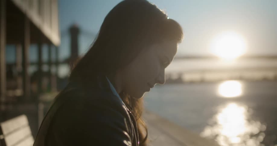 A woman is standing outdoors at dusk by an ocean