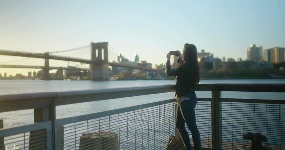 A woman takes a picture of the bridge by the water