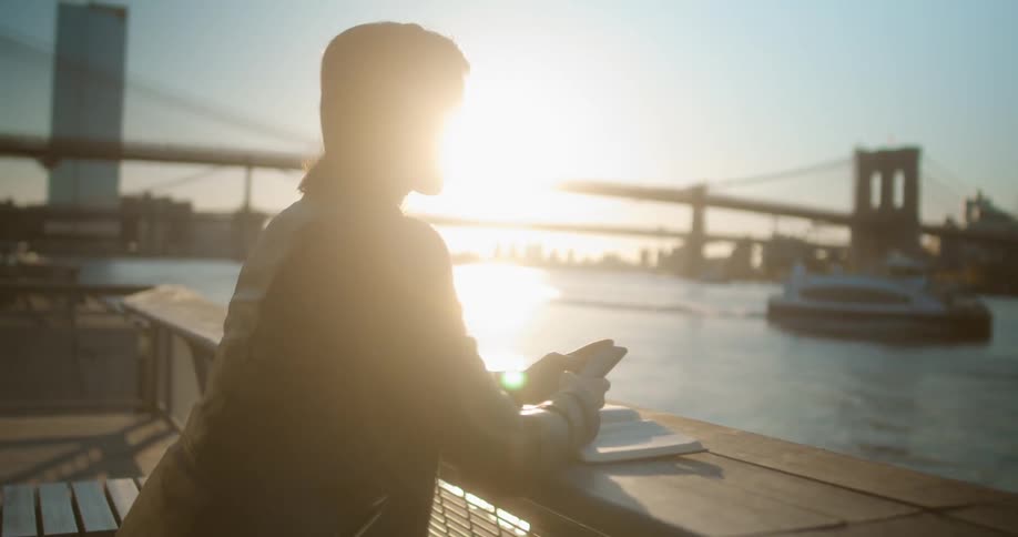 A woman stands on a riverside pier looking at her cell phone