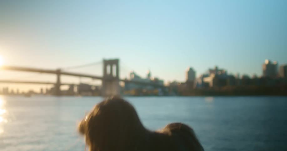 Woman standing across from bridge and city takes sip from cup before pulling up face mask and walking away