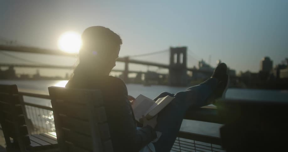 A woman sits on a city river balcony reading a book