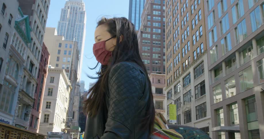 Woman wearing a covid mask walks across the city street as cars sit nearby