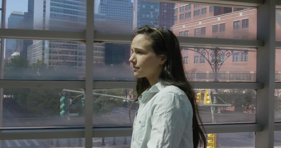 A young woman walks on a pedestrian bridge over a busy intersection downtown