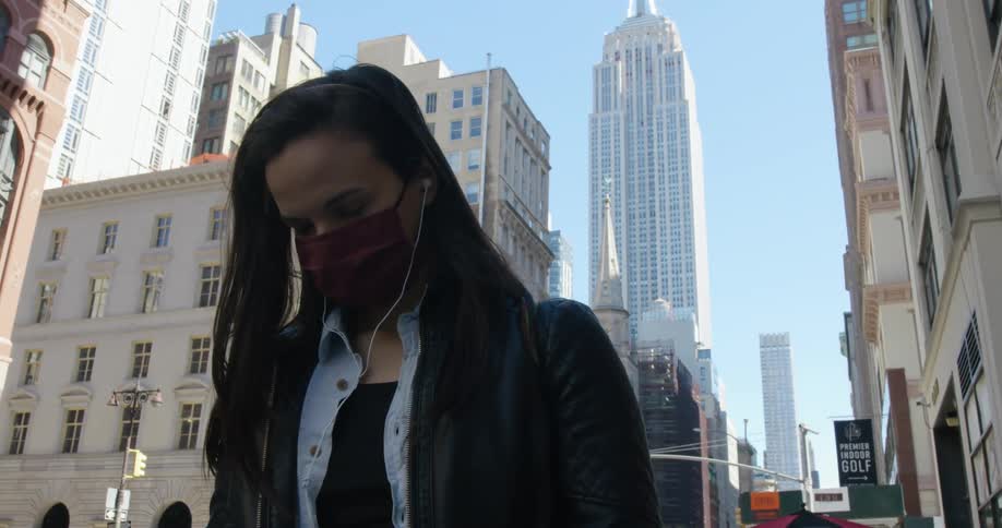 A woman stands in a large city and puts earbuds in her ear