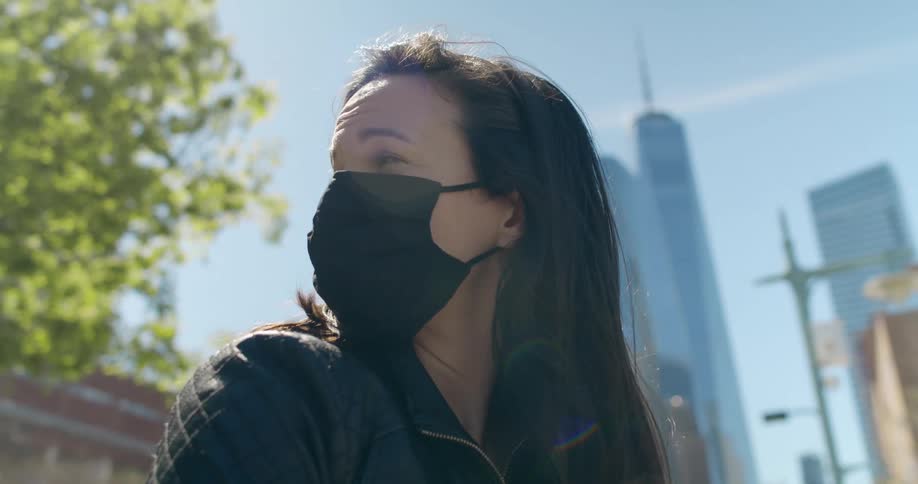 A woman with a face mask outside in a city near tall skyscrapers