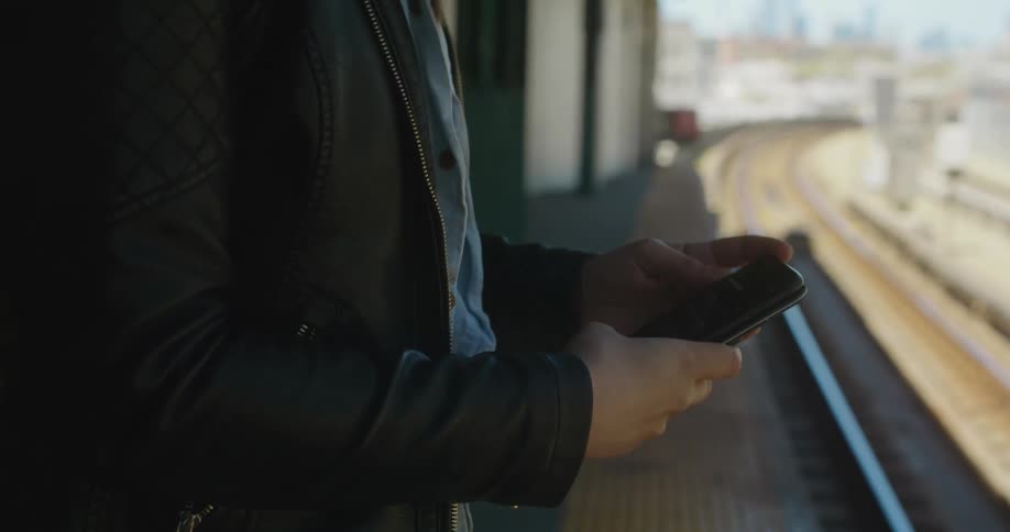 A teenage girl stands above a set of train tracks and looks at her cell phone