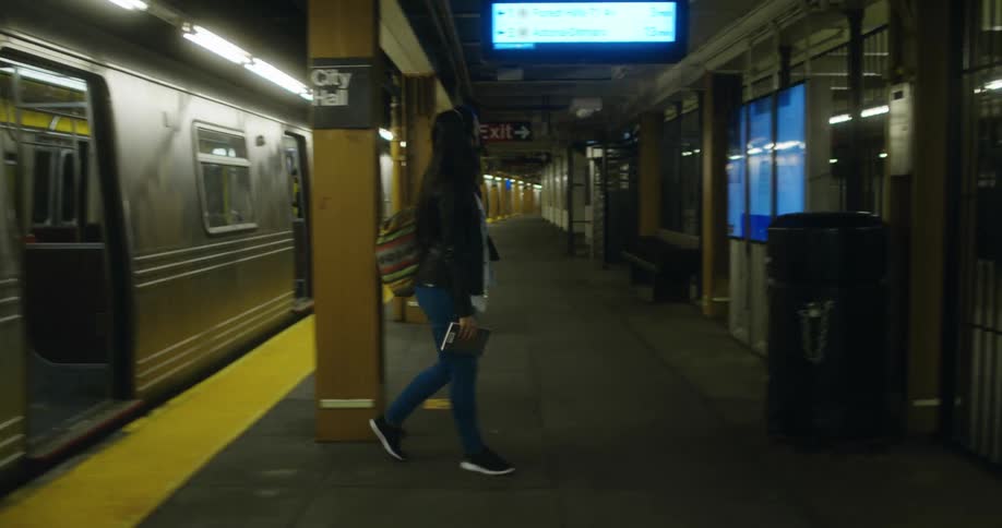 Woman with a black mask a bag a black coat and jeans gets off the subway train