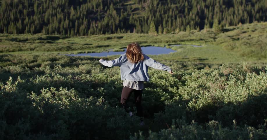 A woman runs down a brush covered hill towards a small pond on a sunny day