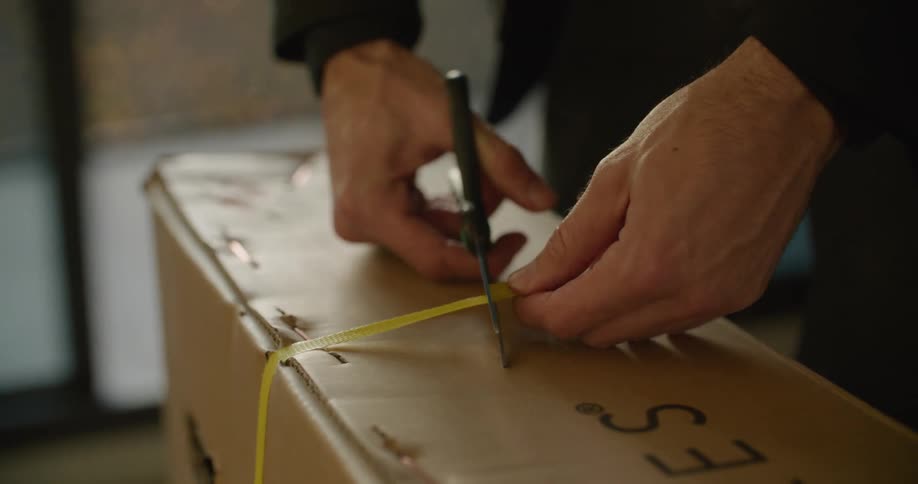 A man cuts the plastic tie off of a cardboard box